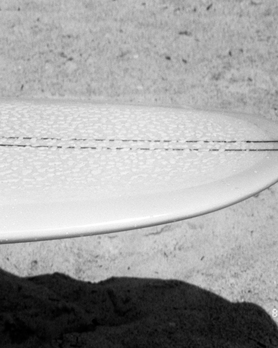 Nez d'une planche de surf couvert de gouttelettes, posé sur le sable