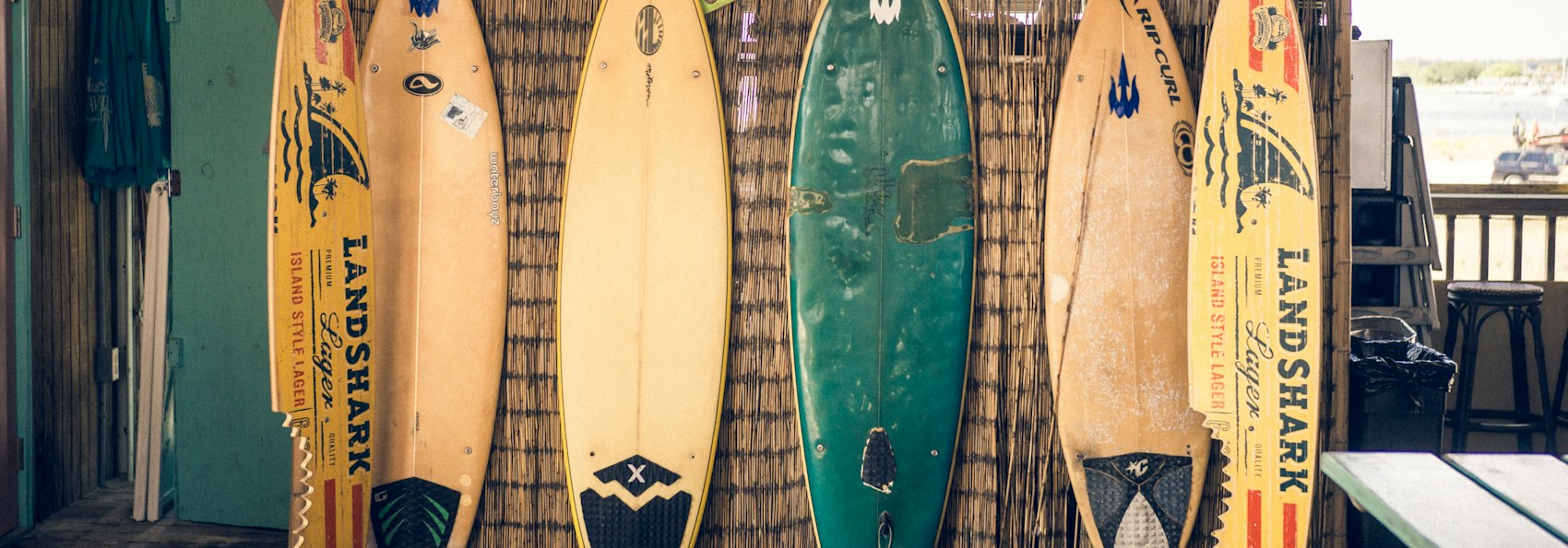 Six planches de surf de couleurs variées alignées contre un mur en bois